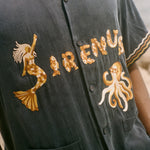 Navy blue shirt with gold embroidery on a blurred beach background