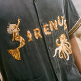 Navy blue shirt with gold embroidery on a blurred beach background