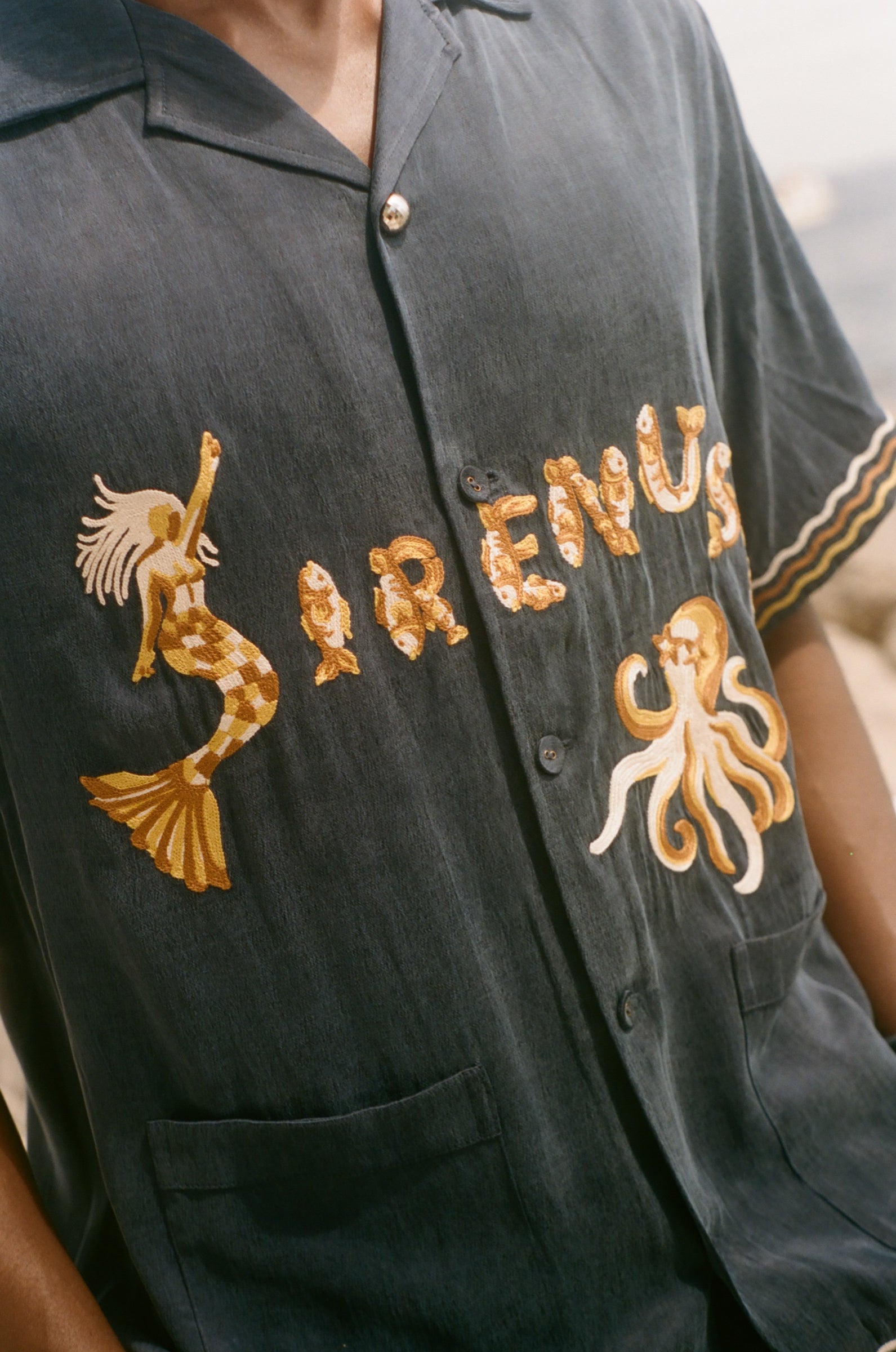 Navy blue shirt with gold embroidery on a blurred beach background
