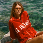 Woman sitting in the sun, wearing the Le Sirenuse Beach Towel top.