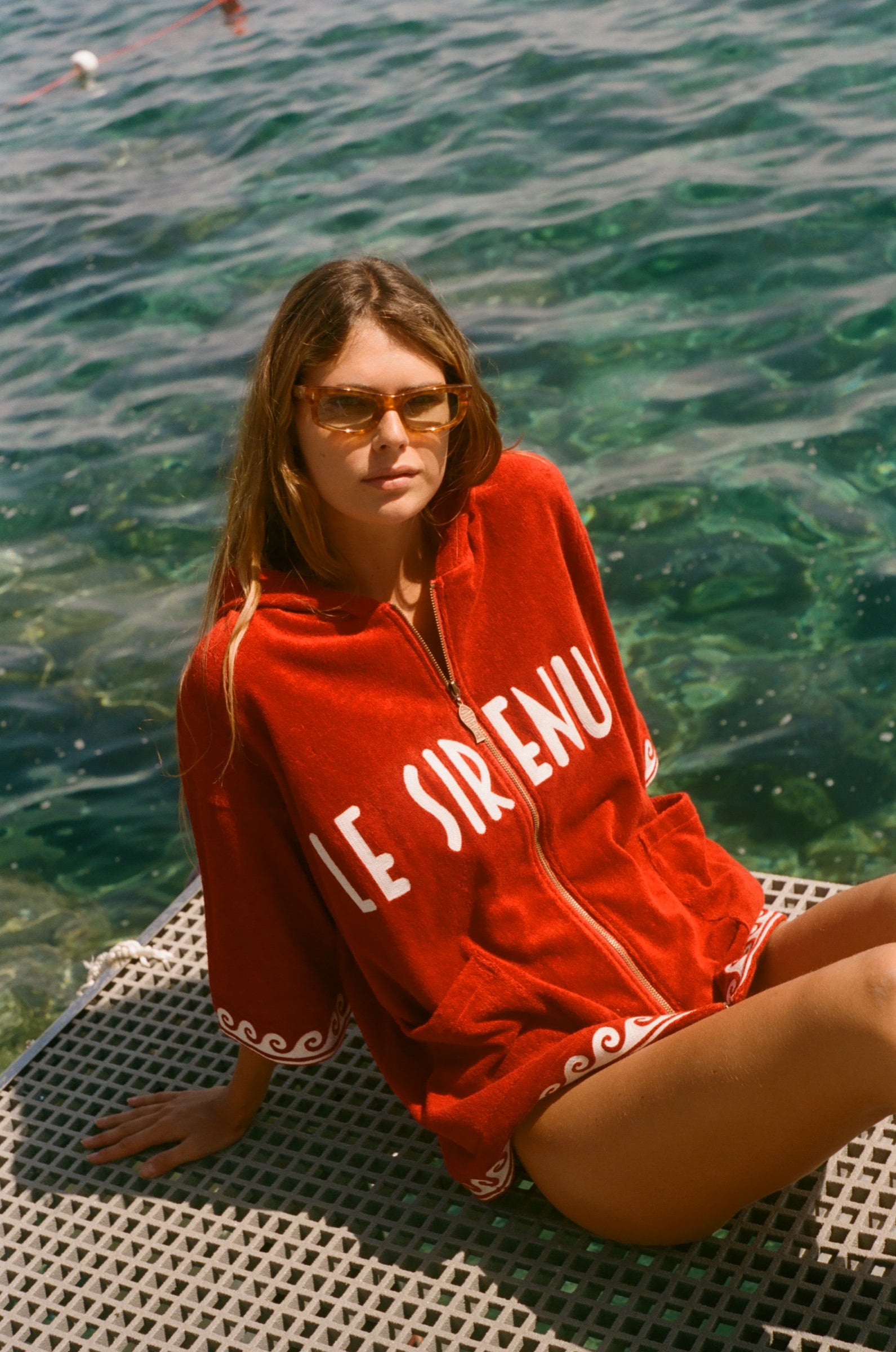 Woman sitting in the sun, wearing the Le Sirenuse Beach Towel top.