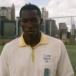 Man wearing a white polo shirt with a yellow collar, featuring FIFA 26 logo.