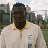 Man wearing a white polo shirt with a yellow collar, featuring FIFA 26 logo.