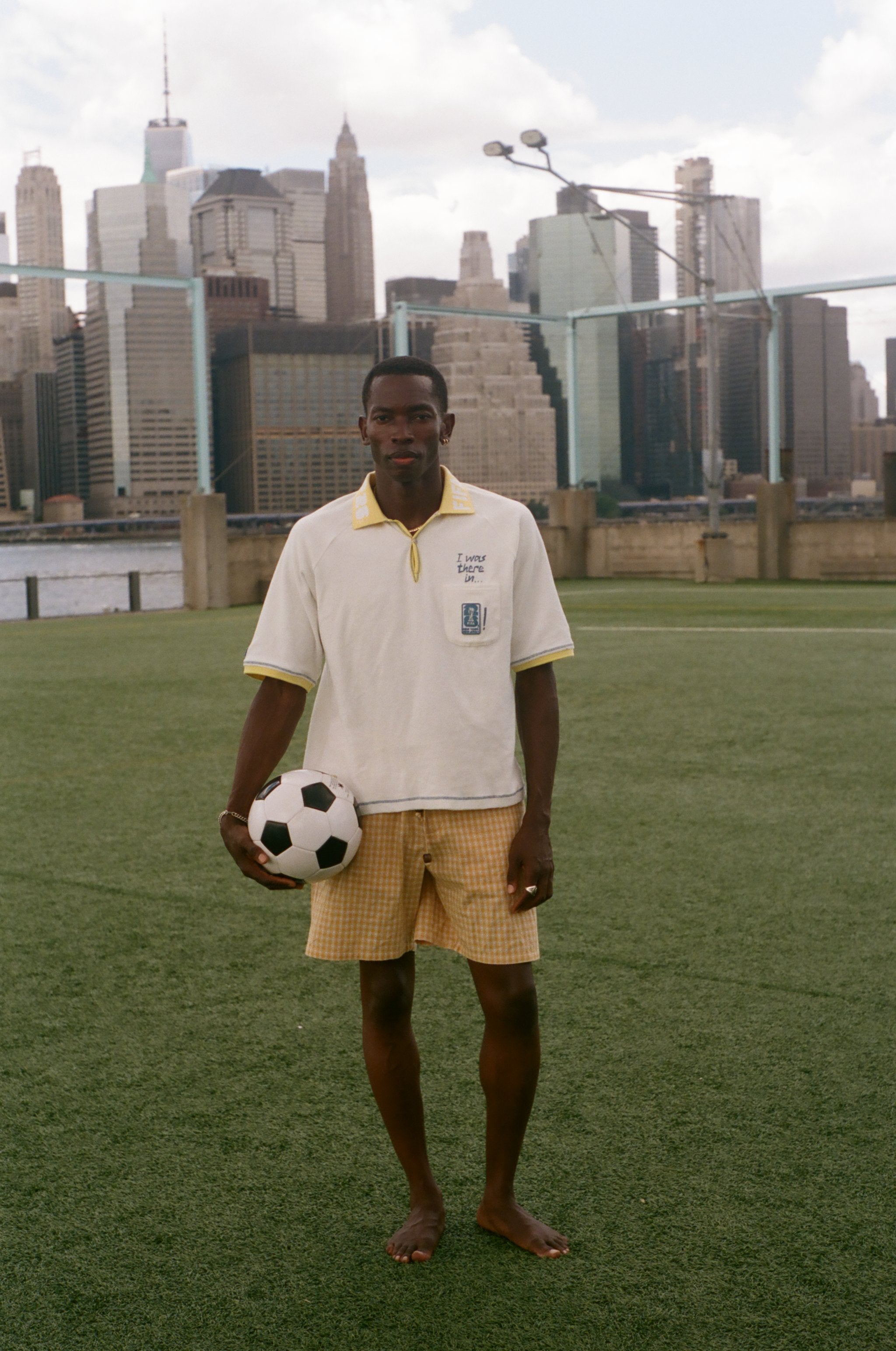 Man holding a soccer ball on a soccer field with a city skyline in the background