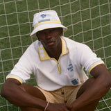 Person wearing a white bucket hat and polo shirt sitting on grass.