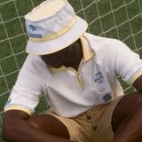 Person wearing a white and yellow outfit with a matching hat, sitting on a soccer field. 