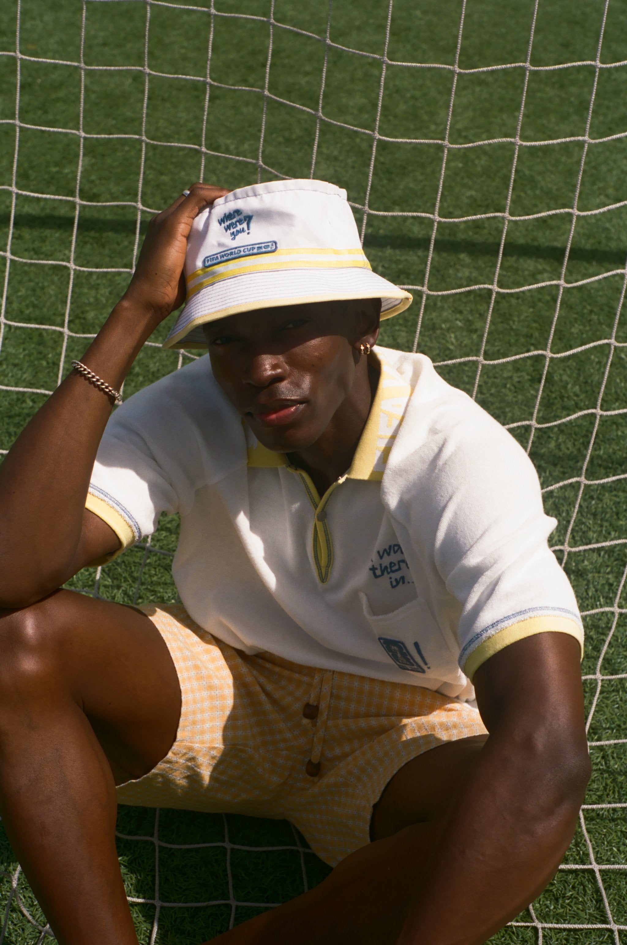 Person wearing a white bucket hat and white polo shirt with yellow accents, sitting on grass.