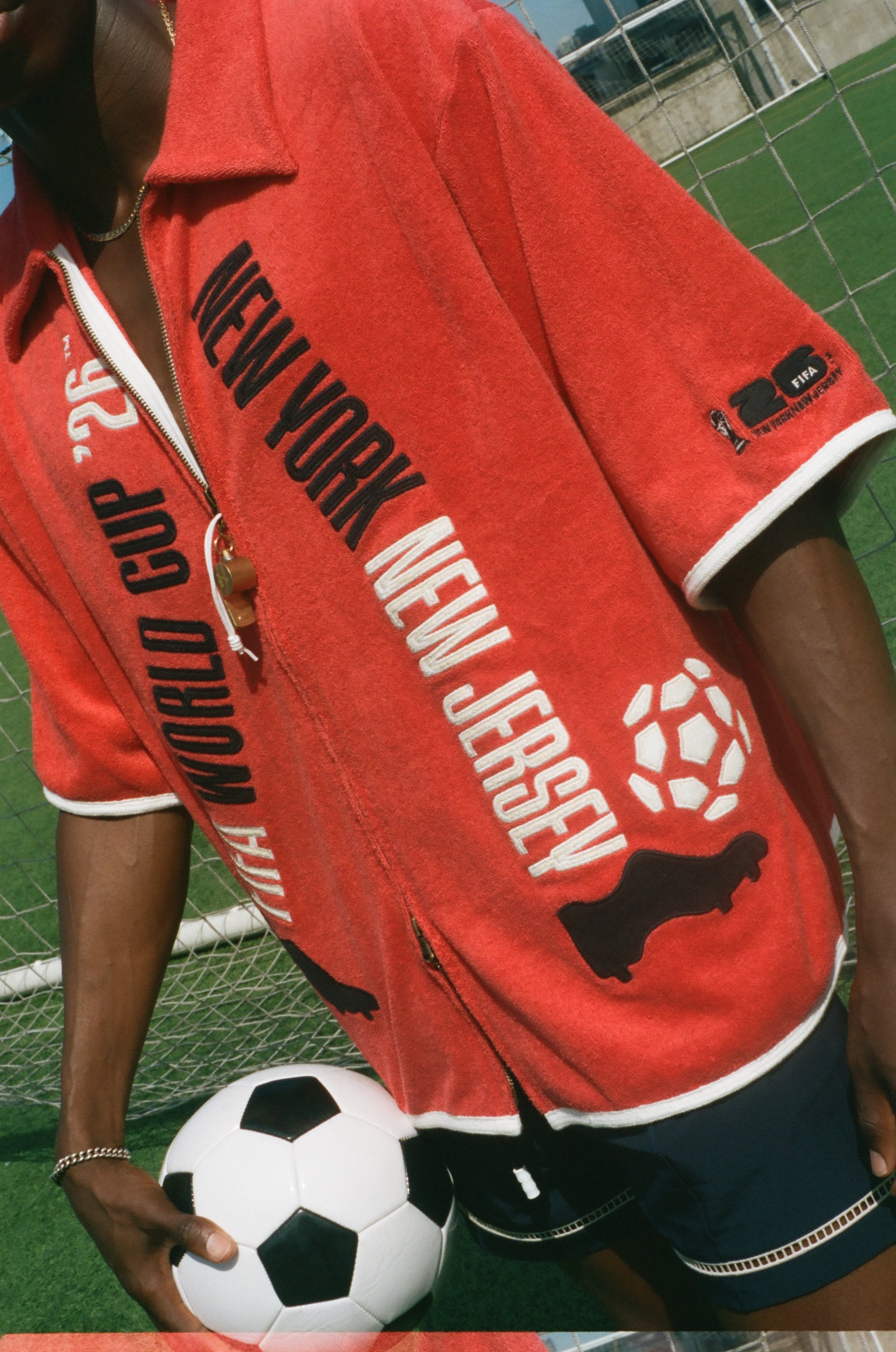 Person wearing a red 'New York New Jersey' World Cup Cabana holding a soccer ball on a grassy field.