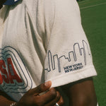 Person wearing a white terry cloth cabana shirt with 'USA' and skyline design on sleeve, standing on a grassy field.