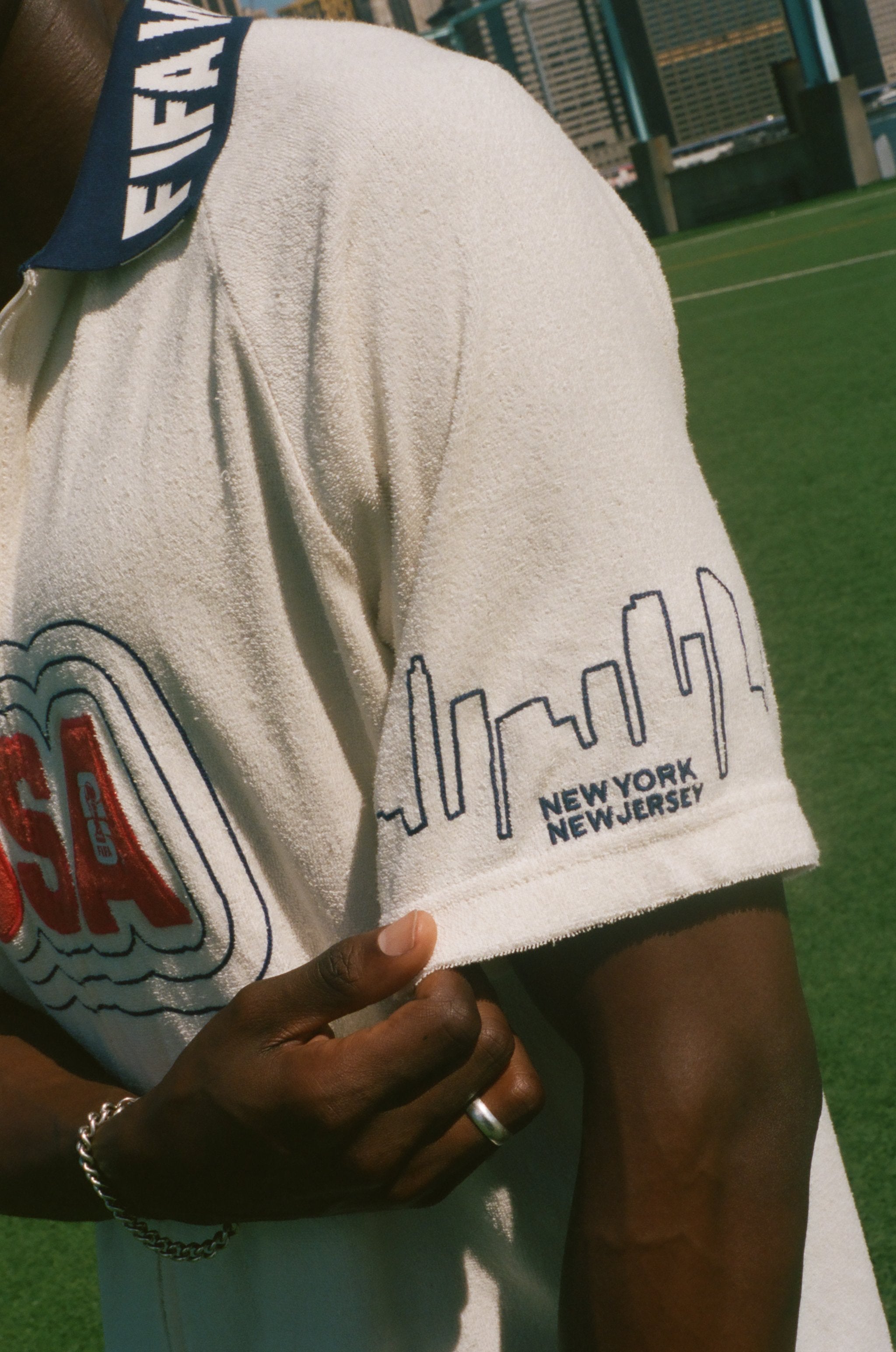 Person wearing a white terry cloth cabana shirt with 'USA' and skyline design on sleeve, standing on a grassy field.