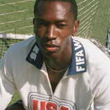 Person wearing a white cabana shirt with 'USA' and FIFA logo on a grass field.
