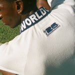 Man sitting on soccer field, showing the back of his USA cabana, which features the FIFA World Cup 2026 logo.