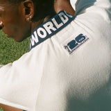 Man sitting on soccer field, showing the back of his USA cabana, which features the FIFA World Cup 2026 logo.