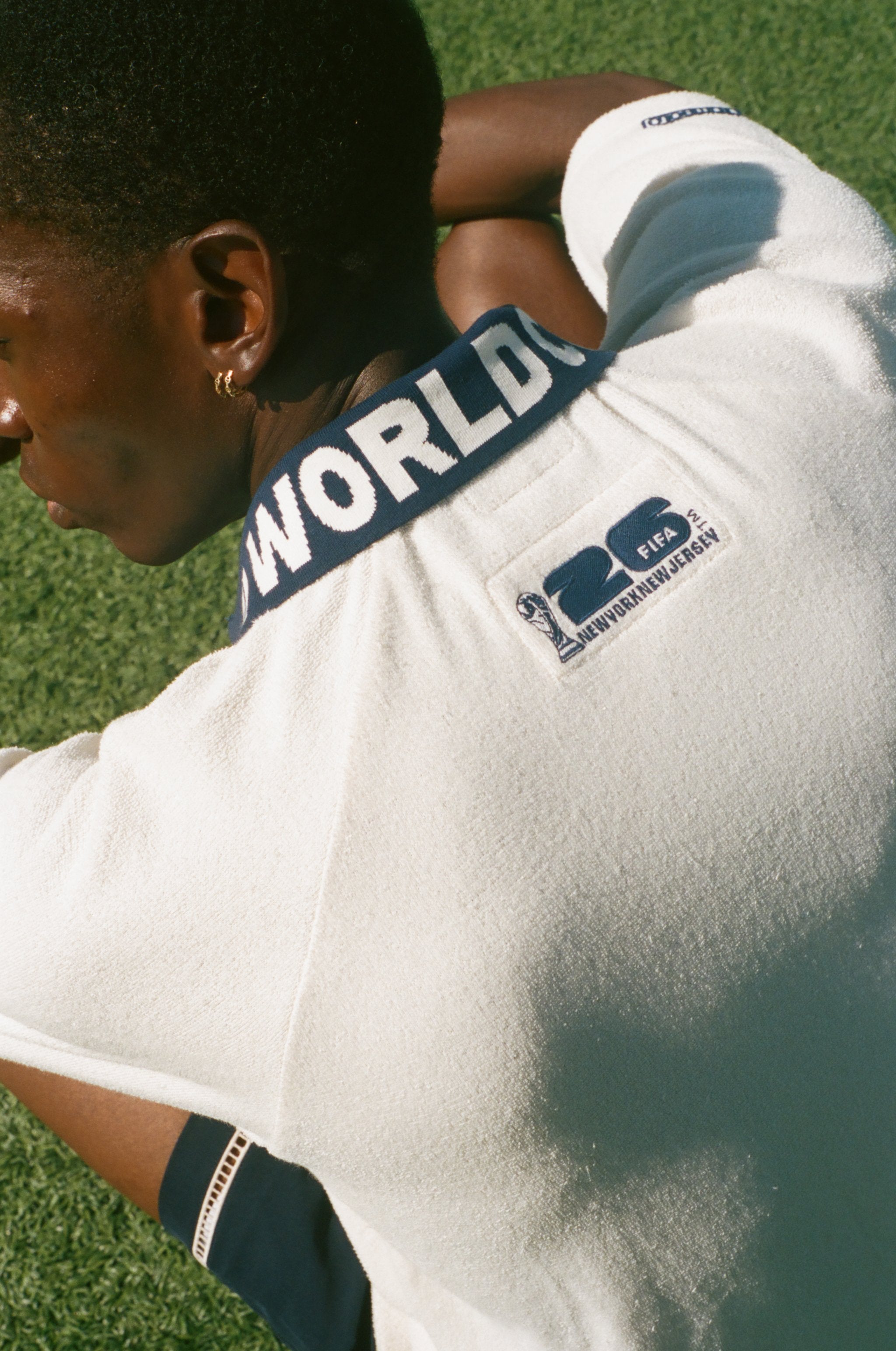 Man sitting on soccer field, showing the back of his USA cabana, which features the FIFA World Cup 2026 logo.
