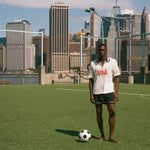 Man standing on a soccer field with a city skyline in the background, wearing a USA terry cloth cabana.