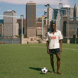 Man standing on a soccer field with a city skyline in the background, wearing a USA terry cloth cabana.