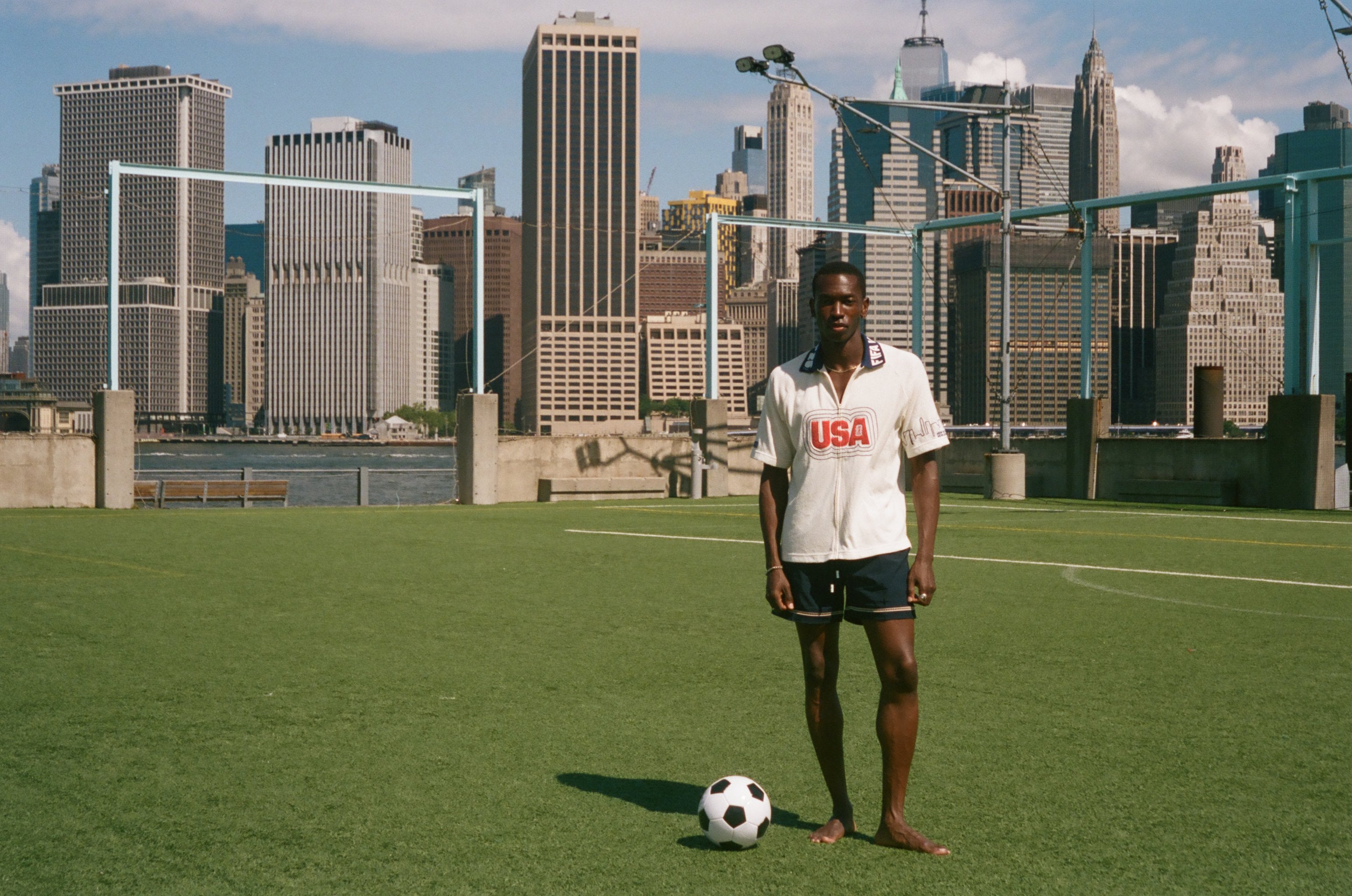 Man standing on a soccer field with a city skyline in the background, wearing a USA terry cloth cabana.