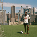 Man standing on a rooftop soccer field with a city skyline in the background, wearing FIFA World Cup USA Cabana. 