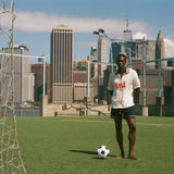 Man standing on a rooftop soccer field with a city skyline in the background, wearing FIFA World Cup USA Cabana. 