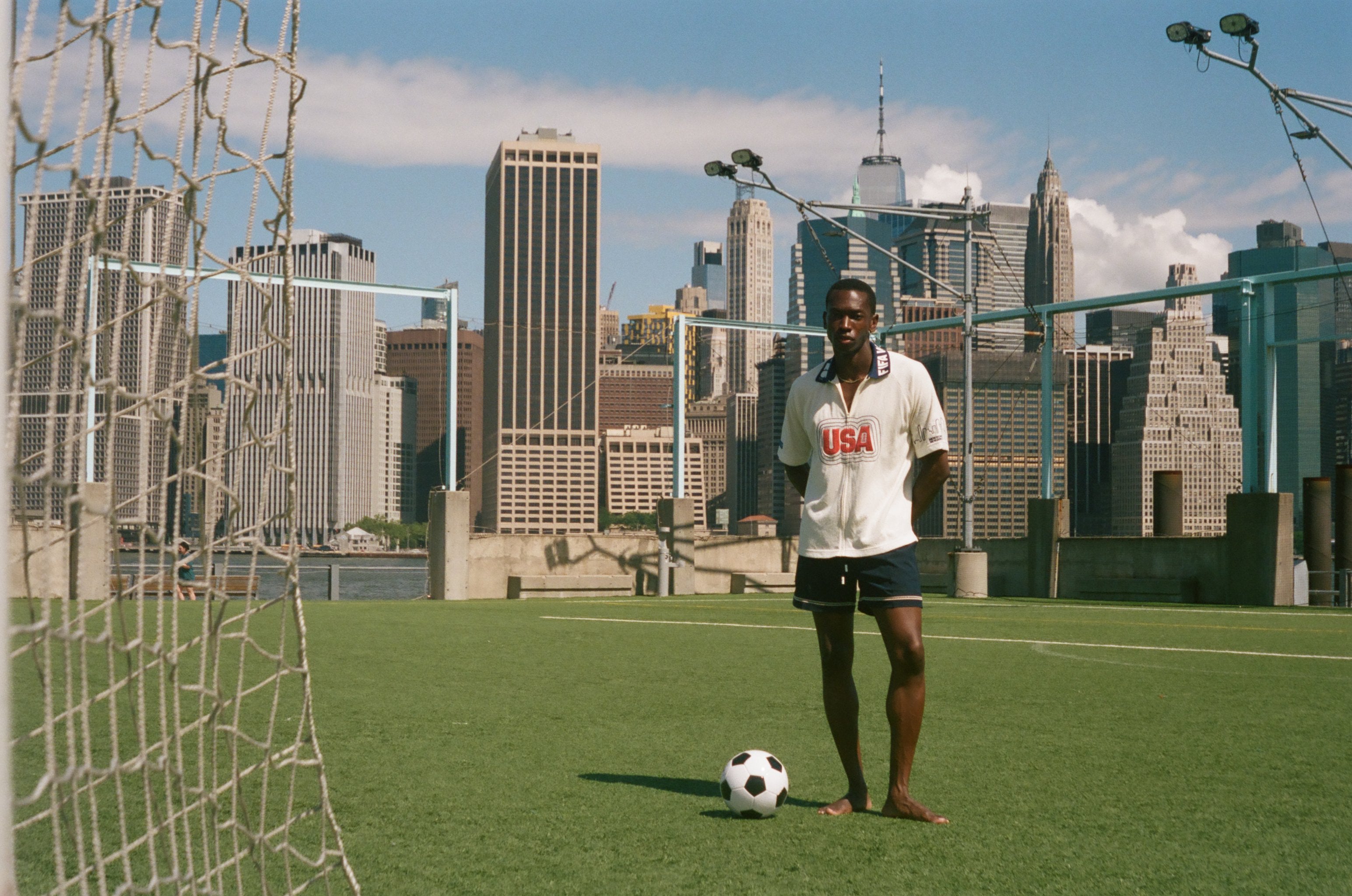 Man standing on a rooftop soccer field with a city skyline in the background, wearing FIFA World Cup USA Cabana. 
