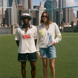 Two people standing on a grassy area with a city skyline in the background, wearing items from the FIFA and Tombolo collection.