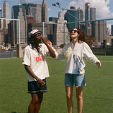 Two people standing on a grassy area with a city skyline in the background, wearing items from the FIFA and Tombolo collection.