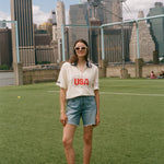 Person wearing a 'USA' cabana shirt on a soccer field with city skyline in the background