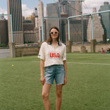Person wearing a 'USA' cabana shirt on a soccer field with city skyline in the background
