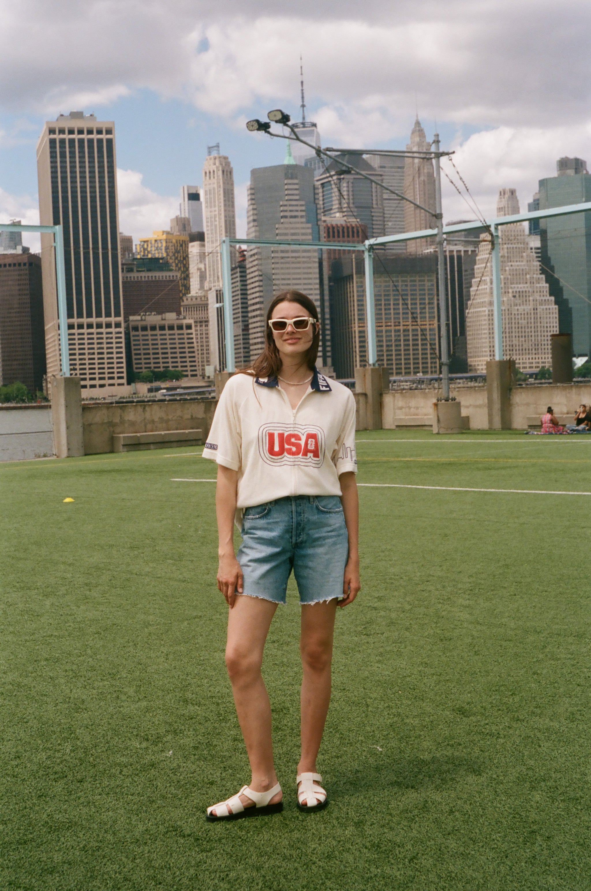 Person wearing a 'USA' cabana shirt on a soccer field with city skyline in the background