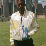 Person wearing a white jacket with a graphic statue of liberty on the front on a sports field with city skyline in the background