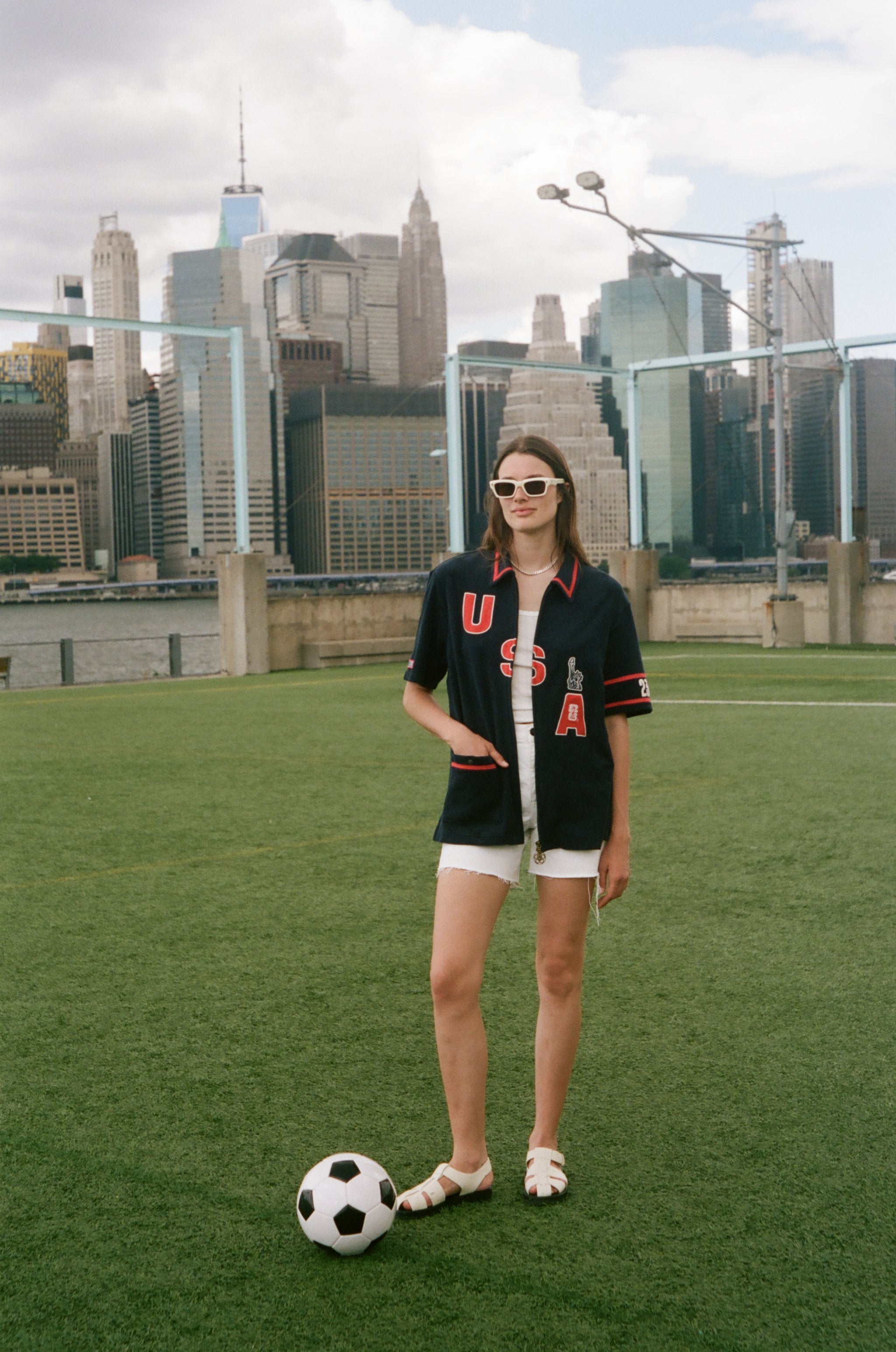 Person wearing a 'USA' cabana with a soccer ball on a soccer field with city skyline in the background