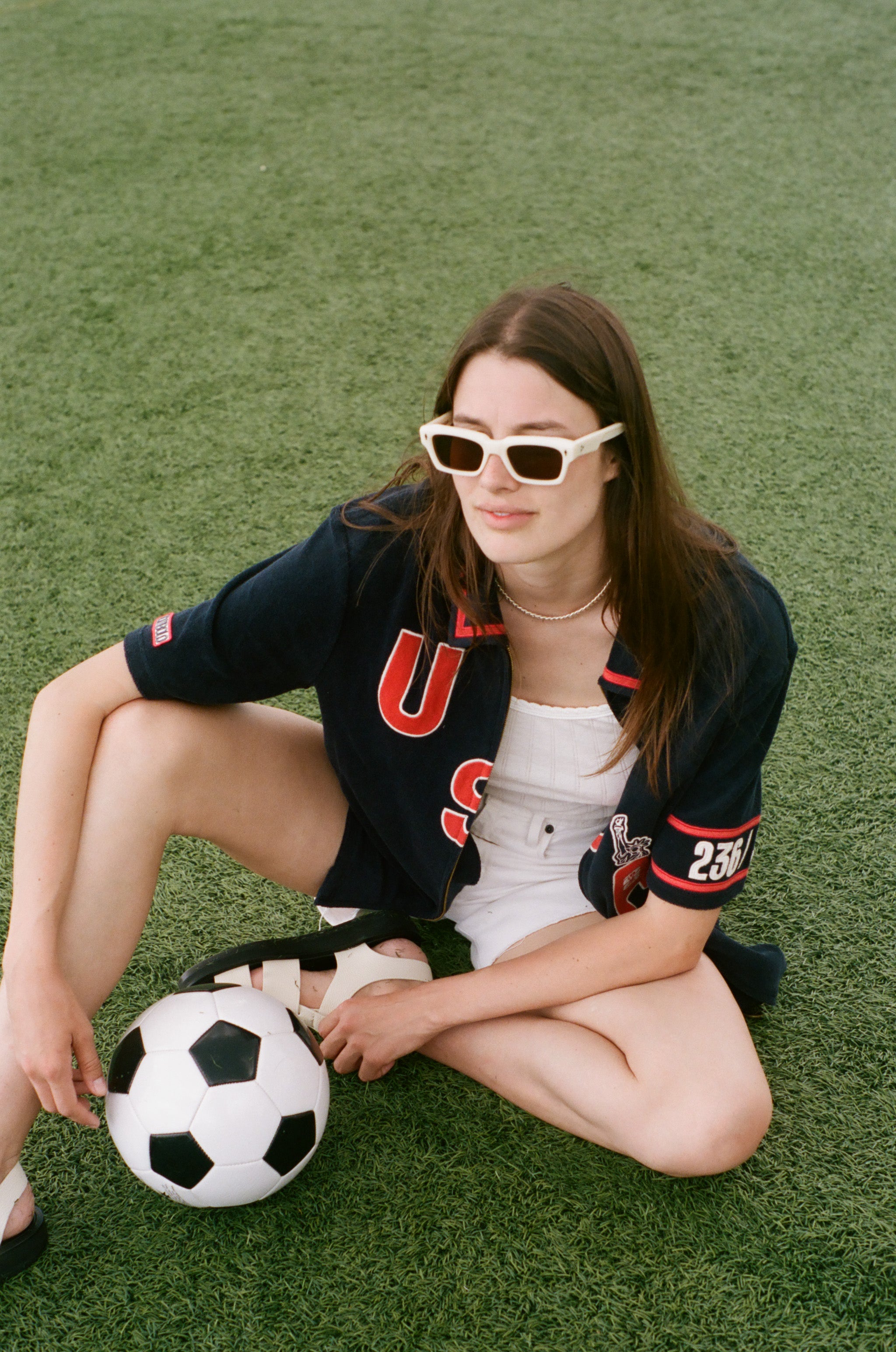 Woman sitting on grass with a soccer ball, wearing sunglasses and a navy USA FIFA cabana from the Tombolo and FIFA collection.