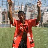 Man wearing red FIFA fancy footwork cabana, standing in front of a soccer net.