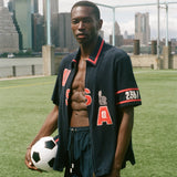Man holding a soccer ball on a sports field with city skyline in the background