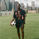 Man holding a soccer ball on a sports field with a city skyline in the background