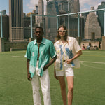 Two people standing on a soccer field, wearing the Teal Stars and Stripes Cabana and the Lady Liberty Hawaiian shirt from the FIFA and Tombolo collection.