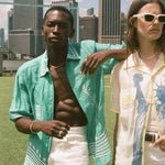 Two people standing in a grassy area with a city skyline in the background, wearing items from the Tombolo and FIFA collection.