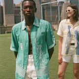 Two people standing on a soccer field, wearing the Teal Stars and Stripes Cabana and the Lady Liberty Hawaiian shirt from the FIFA and Tombolo collection.