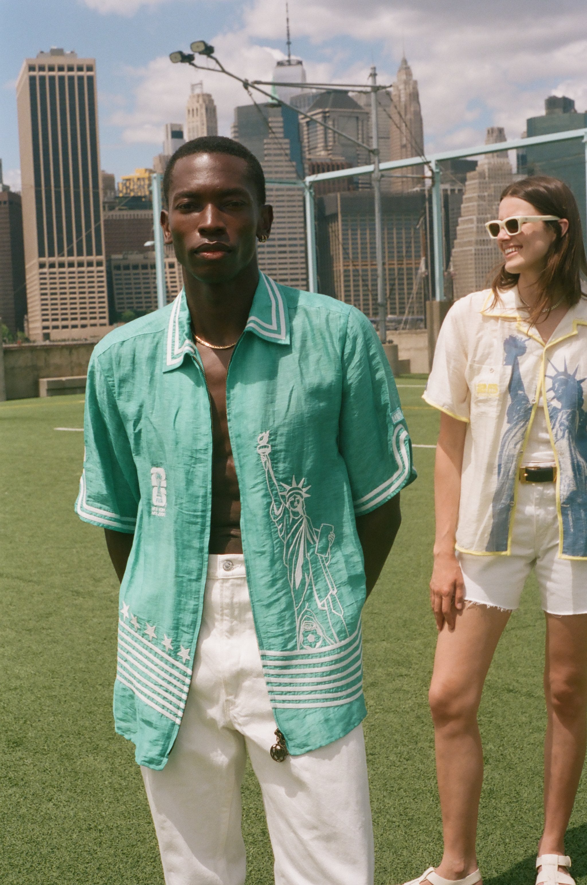 Two people standing on a soccer field, wearing the Teal Stars and Stripes Cabana and the Lady Liberty Hawaiian shirt from the FIFA and Tombolo collection.