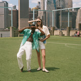 Man and woman standing on a soccer field, looking off into the distance. Both are wearing items from the FIFA and Tombolo collection.