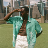 Man wearing the teal Stars and Stripes Cabana with white pants, looking off into the distance on a soccer field. 