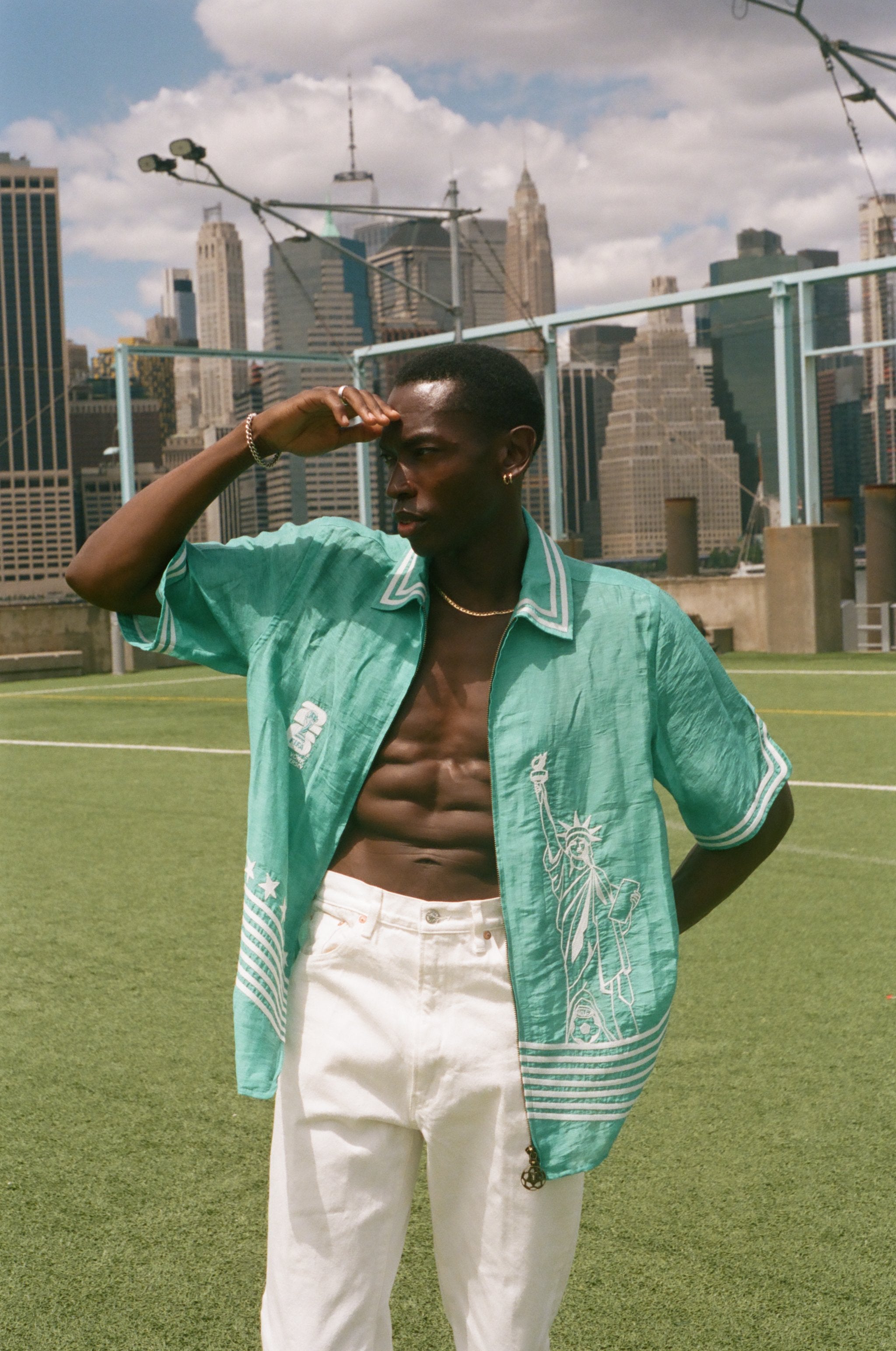 Man wearing the teal Stars and Stripes Cabana with white pants, looking off into the distance on a soccer field. 