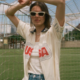 Person wearing sunglasses and a USA cabana shirt in front of a soccer goal.