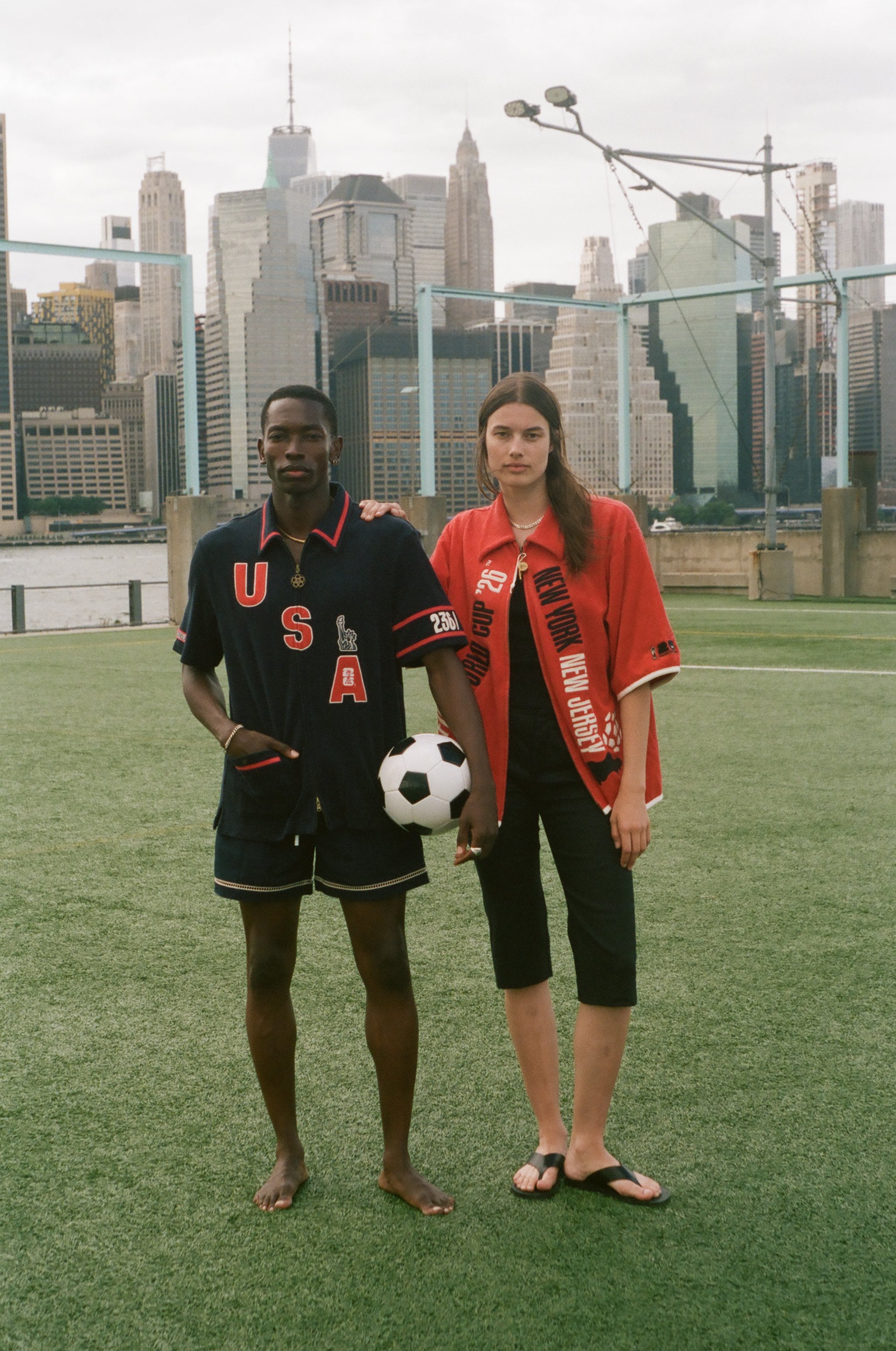 Two people standing on a soccer field with a city skyline in the background