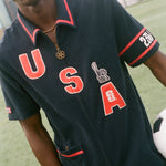 Person wearing a navy cabana shirt with 'USA' printed on it, holding a soccer ball.