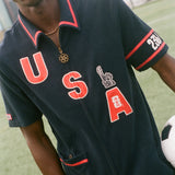 Person wearing a navy cabana shirt with 'USA' printed on it, holding a soccer ball.