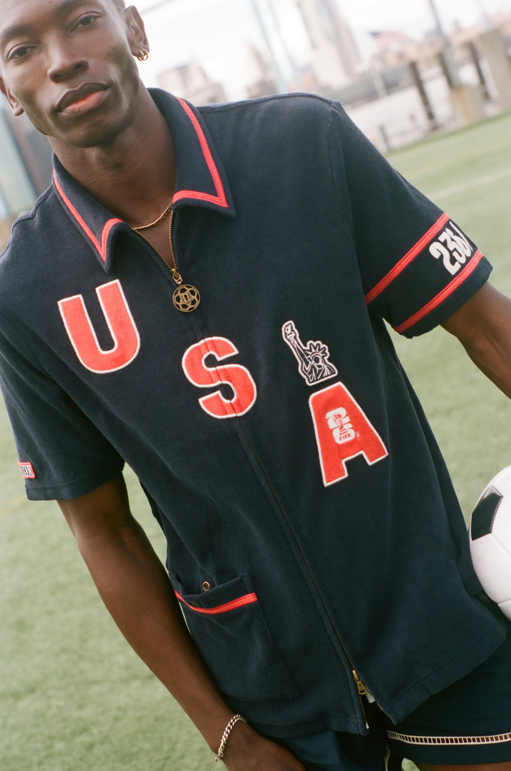 Person wearing a navy cabana shirt with 'USA' printed on it, holding a soccer ball.