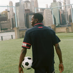 Man facing away from camera, carrying a soccer ball and wearing the navy USA FIFA Cabana.