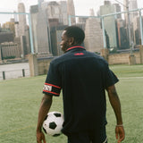 Man facing away from camera, carrying a soccer ball and wearing the navy USA FIFA Cabana.