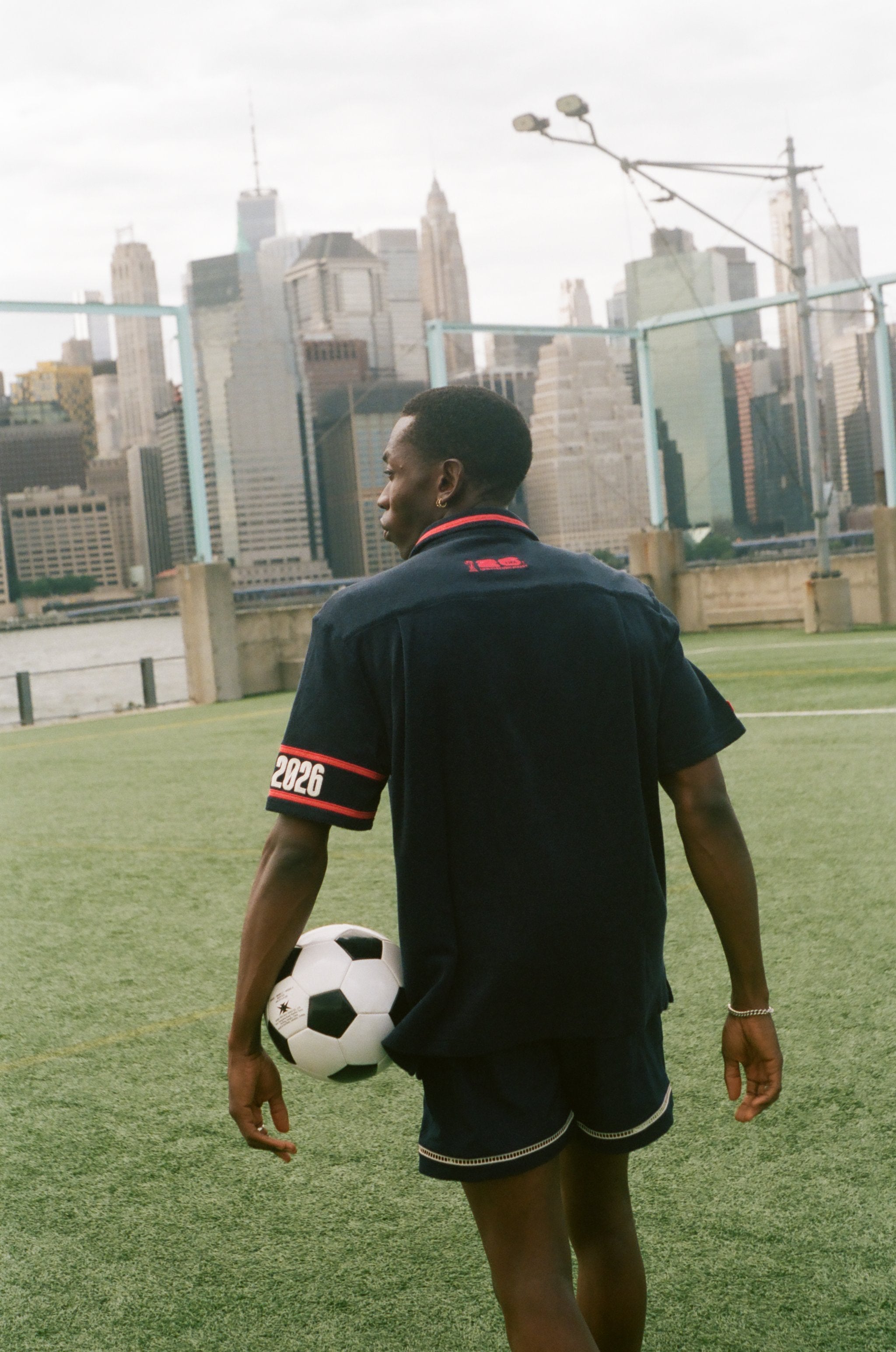 Man facing away from camera, carrying a soccer ball and wearing the navy USA FIFA Cabana.